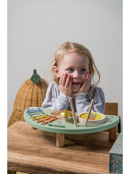 Barn ved træbord med grøn og orange madlegetøj på rund plastiktallerken.