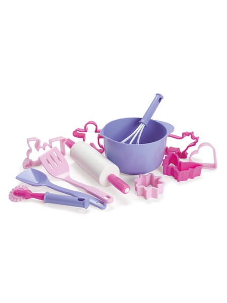 Barn leger med lyserødt bagesæt ved hvidt bord. Småkageudstikkere og andet bageudstyr er spredt på bordet.