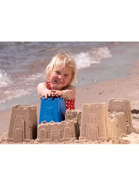 Barn med rød prikket badetøj leger med blå sandslot-skovl på stranden.