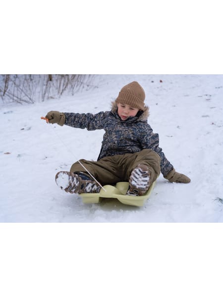 Barn på grøn bobslæde i sneen om vinteren