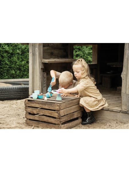 To børn leger med dessert-sæt på en trækasse udendørs under et overdækket område