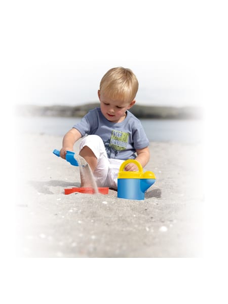 Barn med blå sandskovl ved vandet på en solrig dag