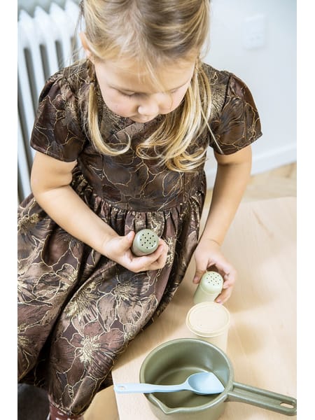 To børn sidder ved et lille bord med legemad og tallerkener i et rum med en radiator på væggen.