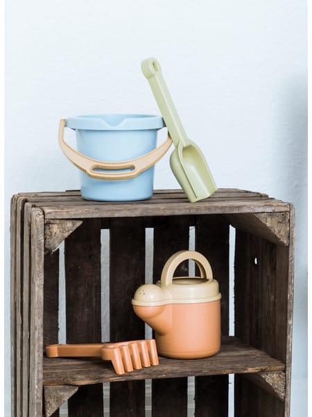 Børnelegetøjssæt med haveredskaber og spand i pastelagtige farver, præsenteret i butikskasse