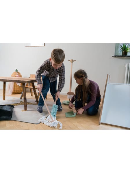 To personer der leger med et rengøringssæt legetøj på et gulv ved en hvid væg.