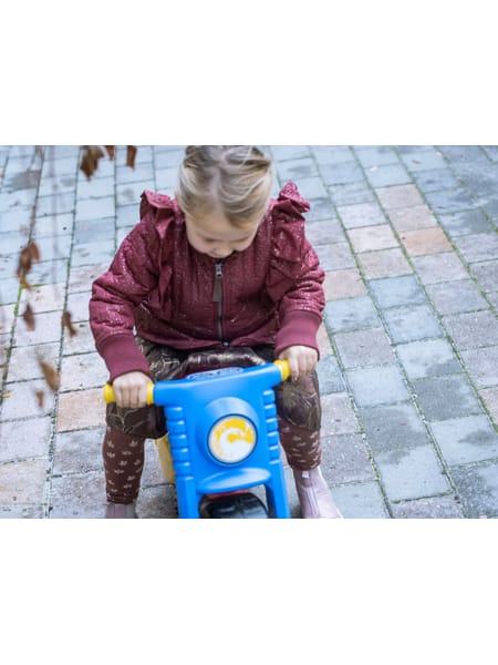 Barn på gul og blå løbecykel på træterrasse ved havemøbler