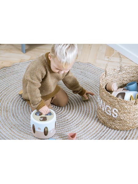 Barn på gulv leger med rund putteboks og tilhørende klodser i naturlige farver