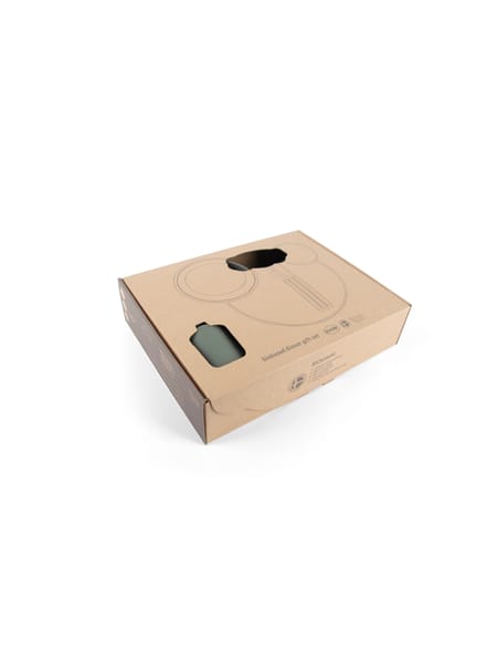 En person holder en kop og tallerken i lyserødt med små grøntsager ved siden af på en grå bakke.