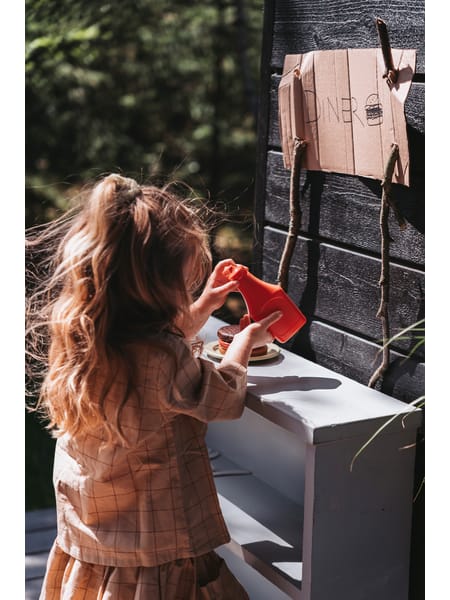 Person med langt hår drikker af kop ved vindue med burgere og drikkevarer på bordet