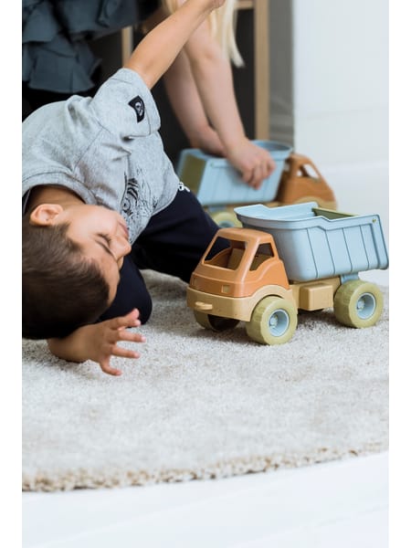 Person ligger på gulvtæppe ved siden af lyseblå og beige legetøjslastbil