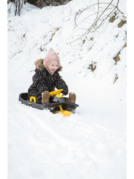 Barn på sort kælk glider ned ad sneklædt bakke