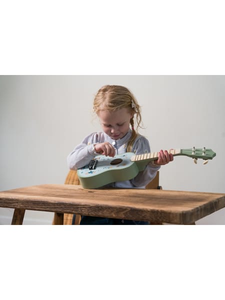 Barn med lille turkis ukulele sidder ved træbord i hjemlig stue