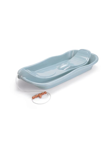 Barn i gul trøje på lyseblå bobslæde med snedækket baggrund.