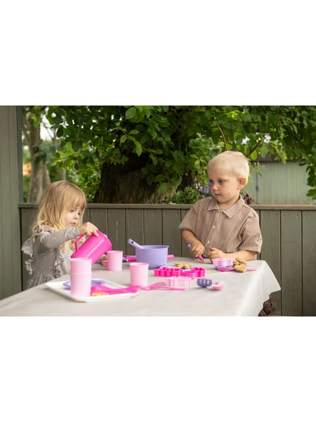 To børn ved lyserødt bord med legetøjskopper og tallerkener til teselskab.