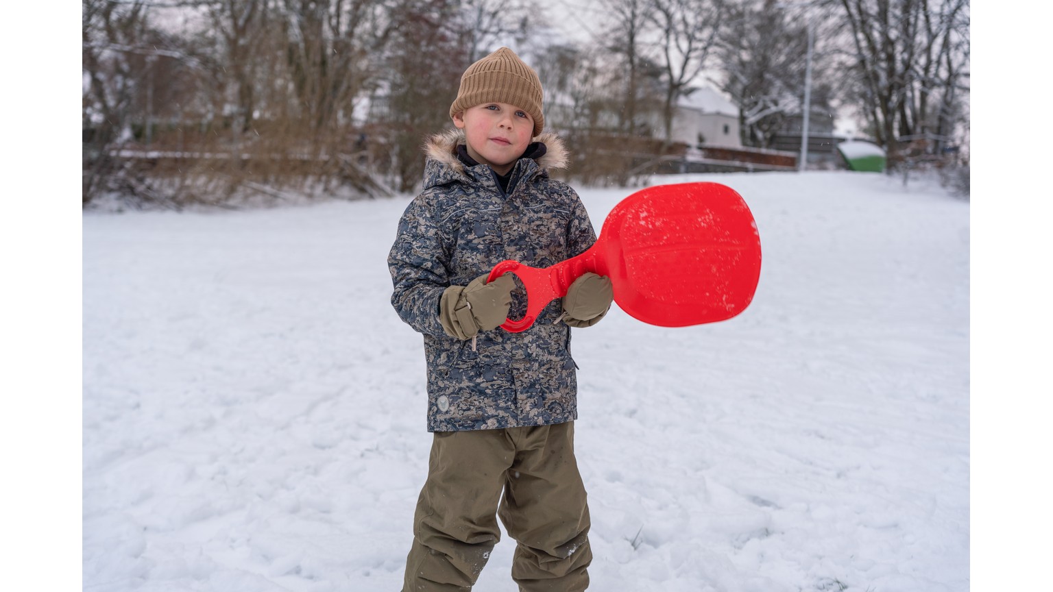 Person med rød kælk på snedækket mark i vintervejr.