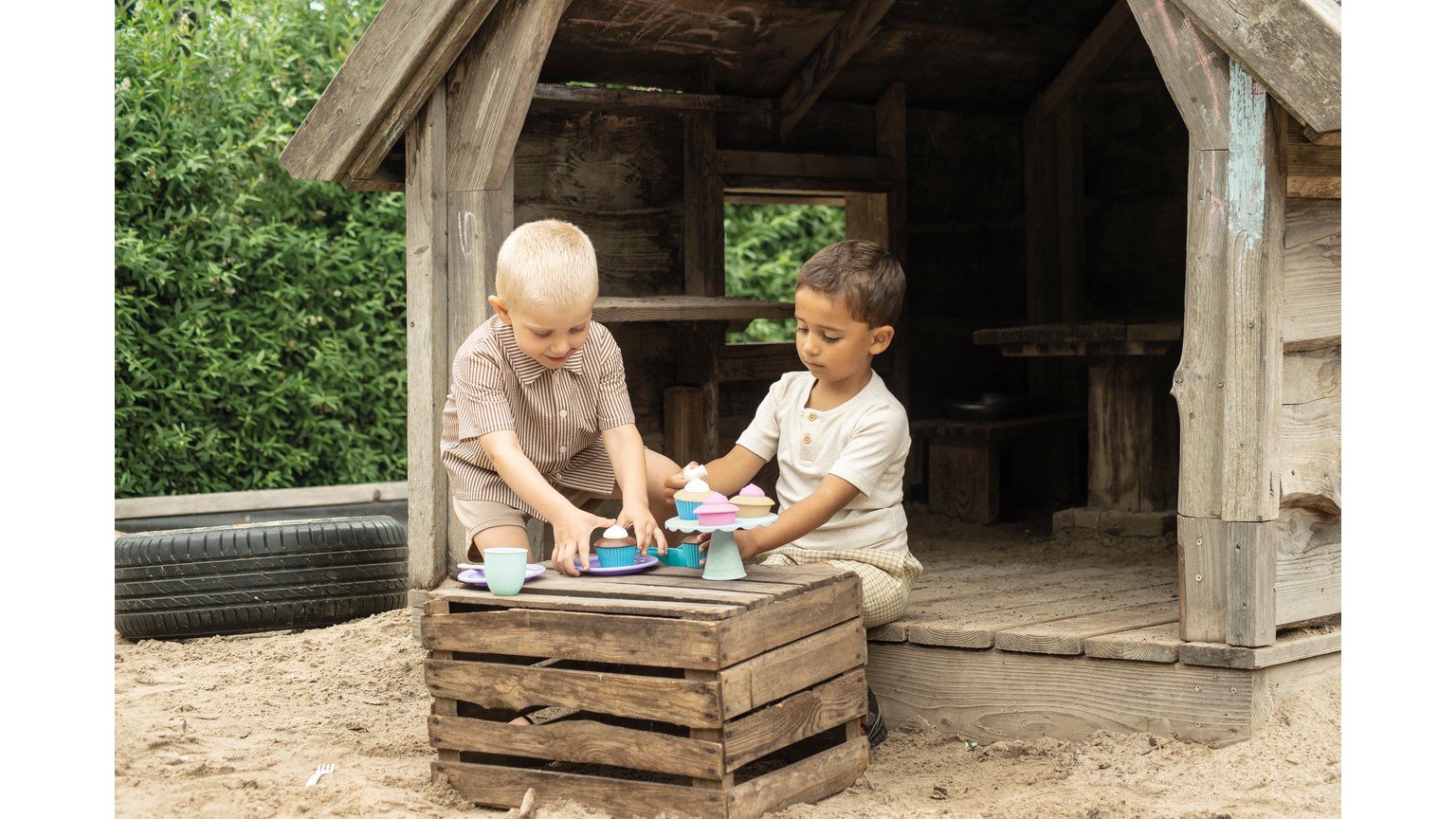 To børn leger med dessert-sæt på en trækasse udendørs under et overdækket område