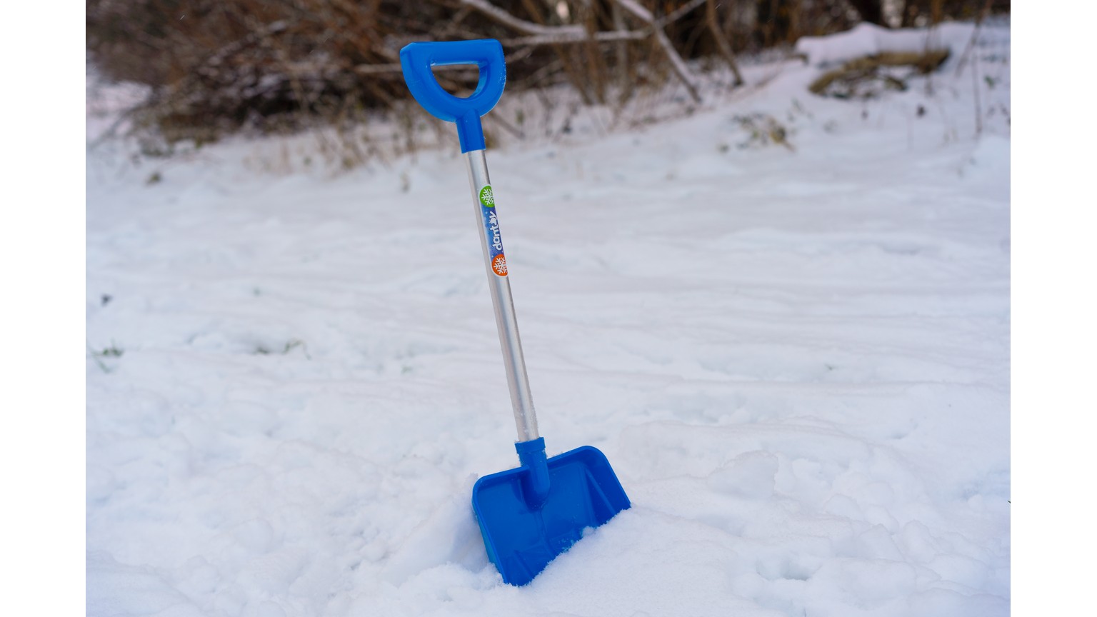 Blå sneskovl med langt håndtag står i snedækket terræn