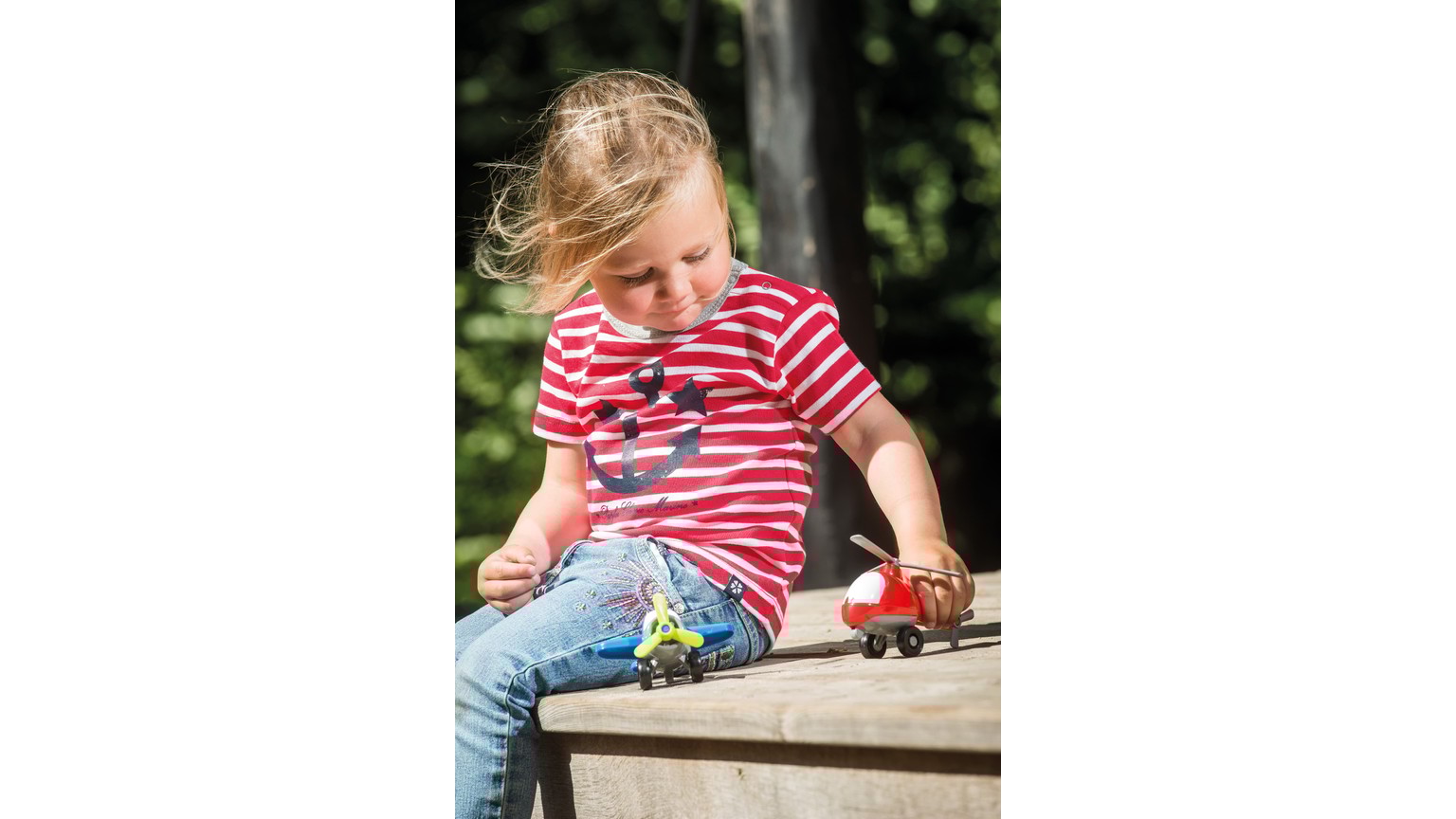 Barn i rødstribet t-shirt leger med små legetøjsbiler på en træoverflade