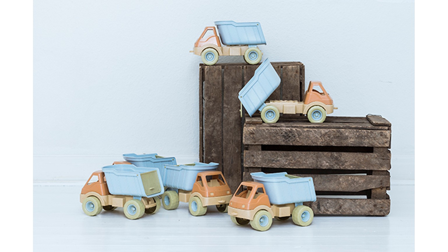 Lyseblå legetøjsbiler placeret ved og på brune trækasser mod en lys baggrund