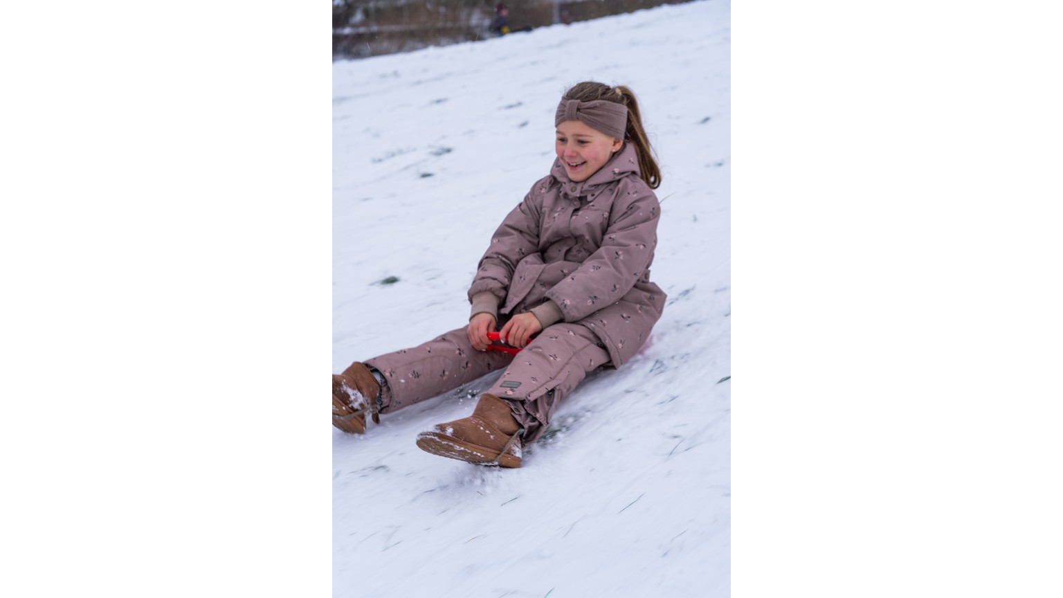 Person på snedækket bakke glider ned på rød kælk i vinterlandskab