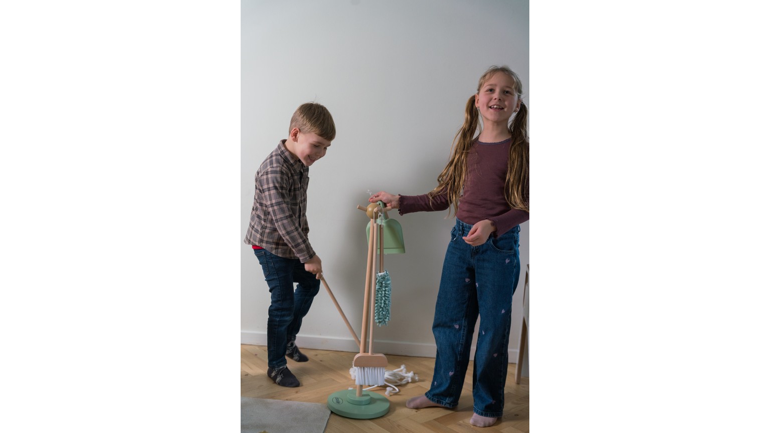 To personer der leger med et rengøringssæt legetøj på et gulv ved en hvid væg.
