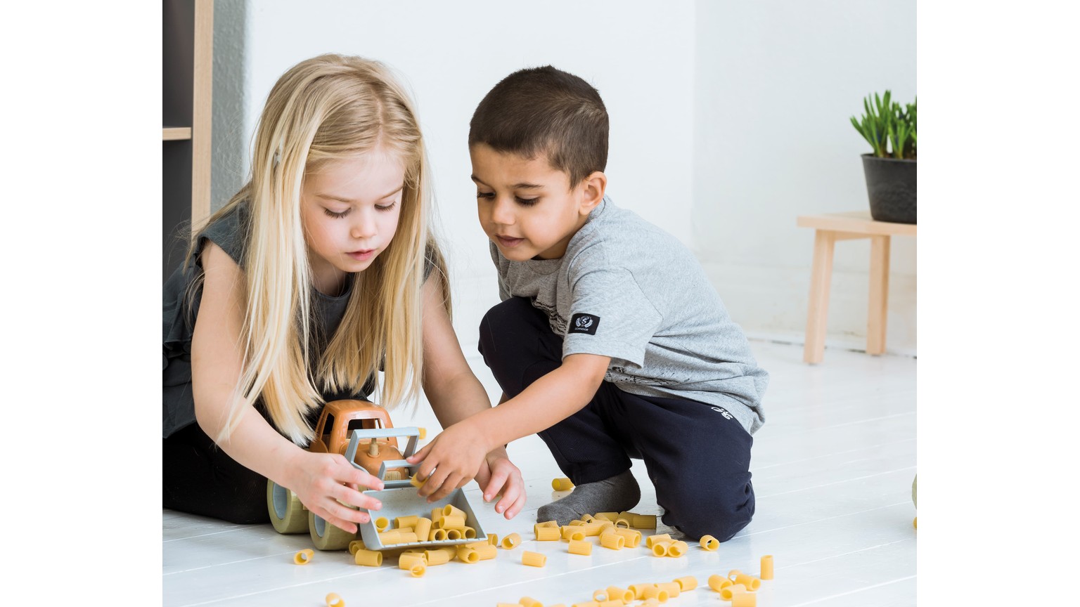 To børn leger på gulvet med gul legetøjstraktor.