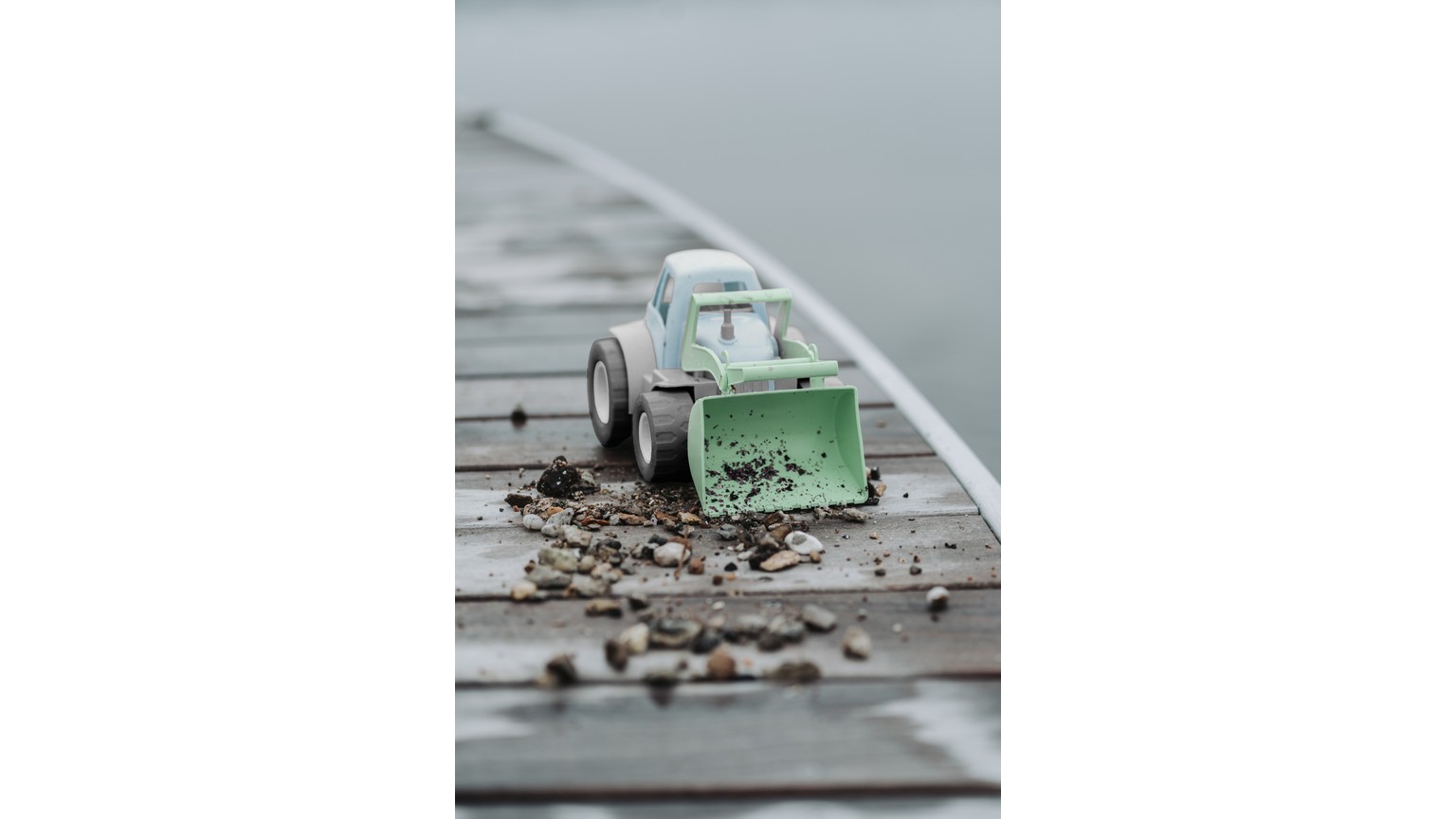 Lille mintgrøn traktor med skovl på våd grå overflade med jordklumper