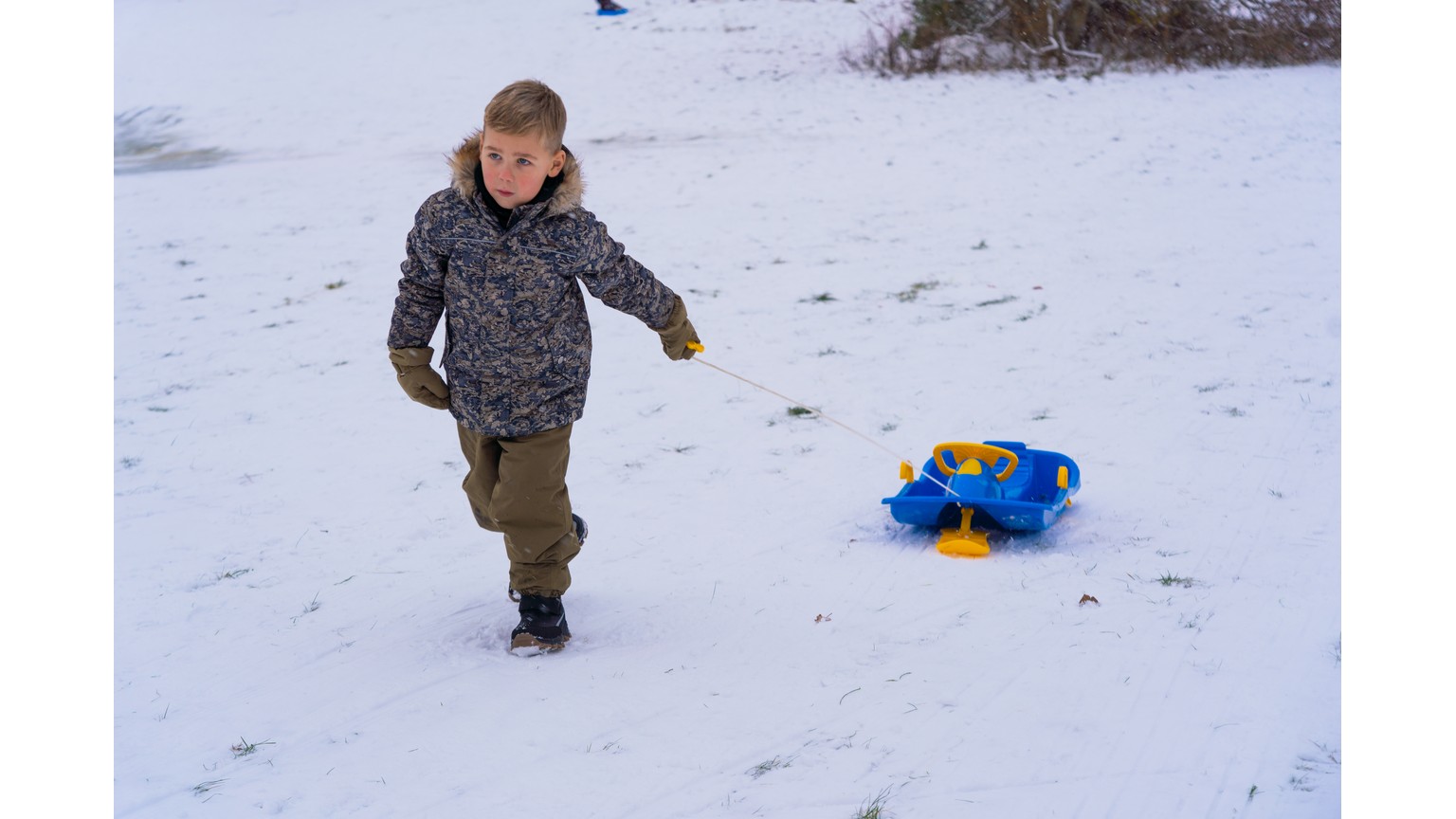 Person leger med blå slæde på snedækket underlag