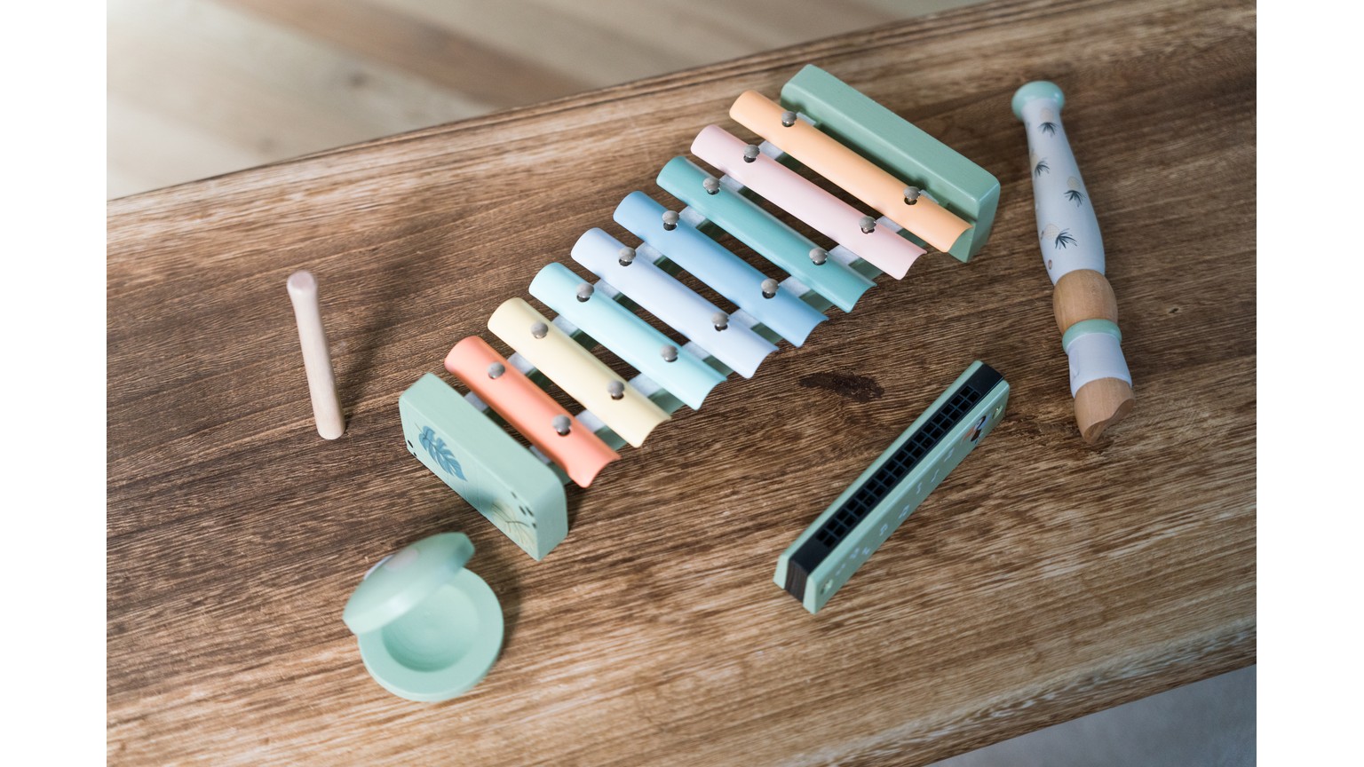 Pastellfarvede musikinstrumenter inklusiv xylofon og fløjte på træbord.