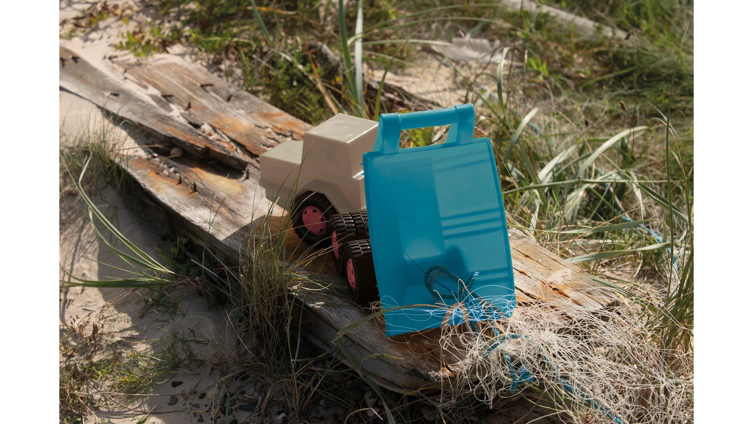 Blå legetøjskøretøj på sandstrand med marehalm.