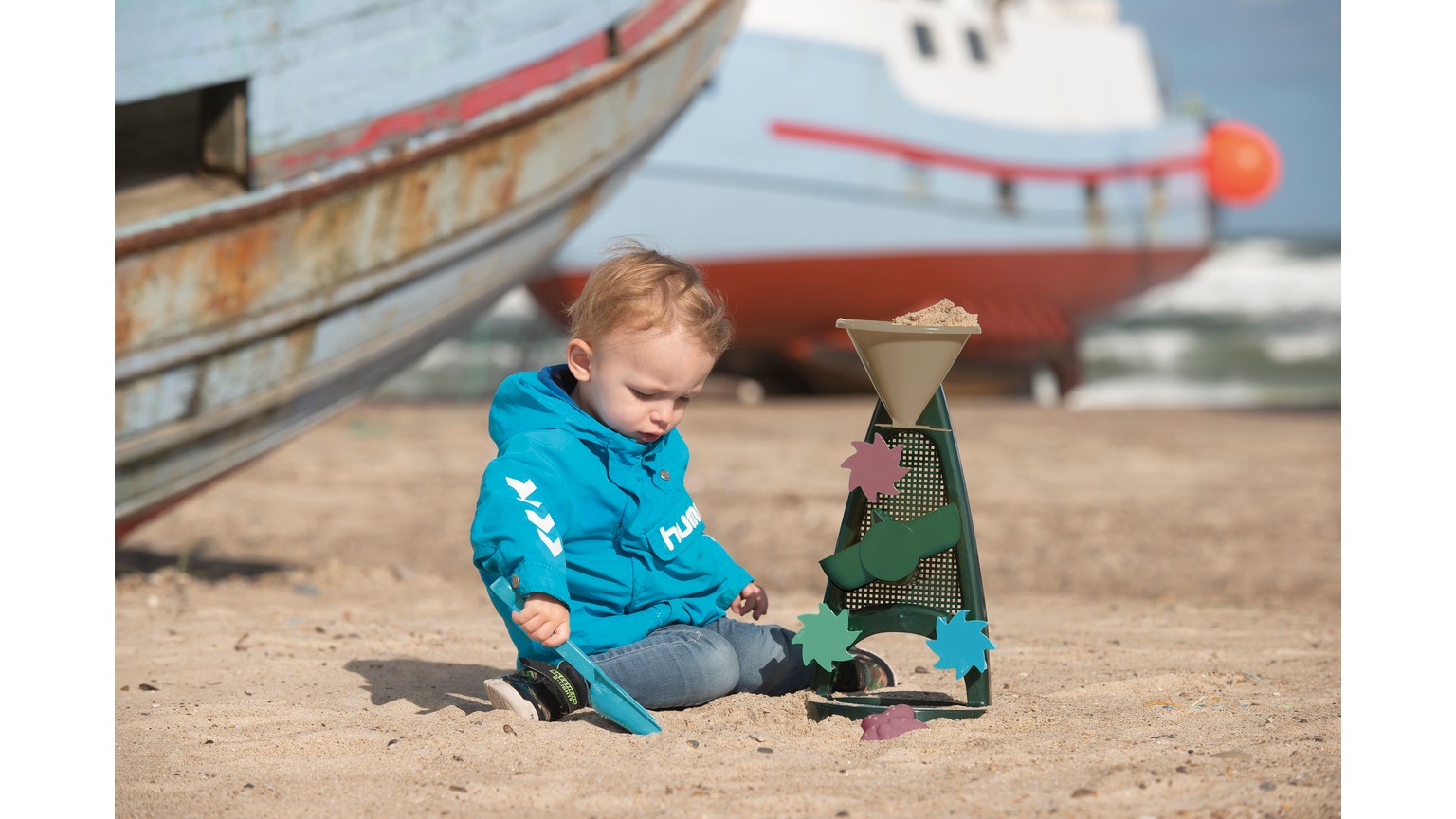 To små figurer på strand ved båd - en i blå dragt og en i grøn dragt leger i sandet