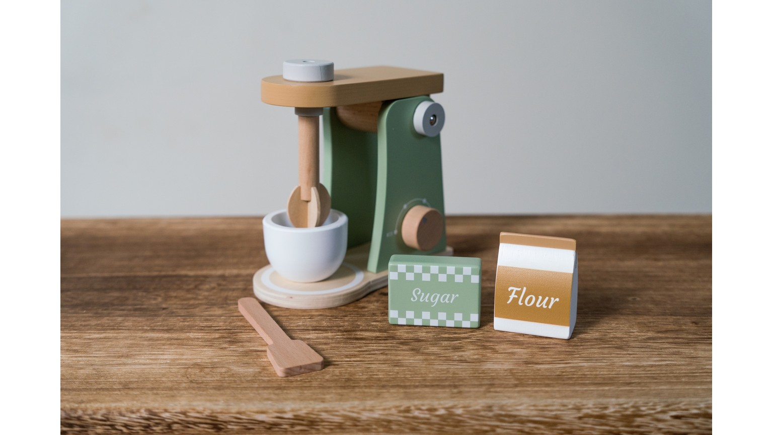 Grøn legetøjsblender med kaffekande og tilbehør på træbord ved siden af krydderier