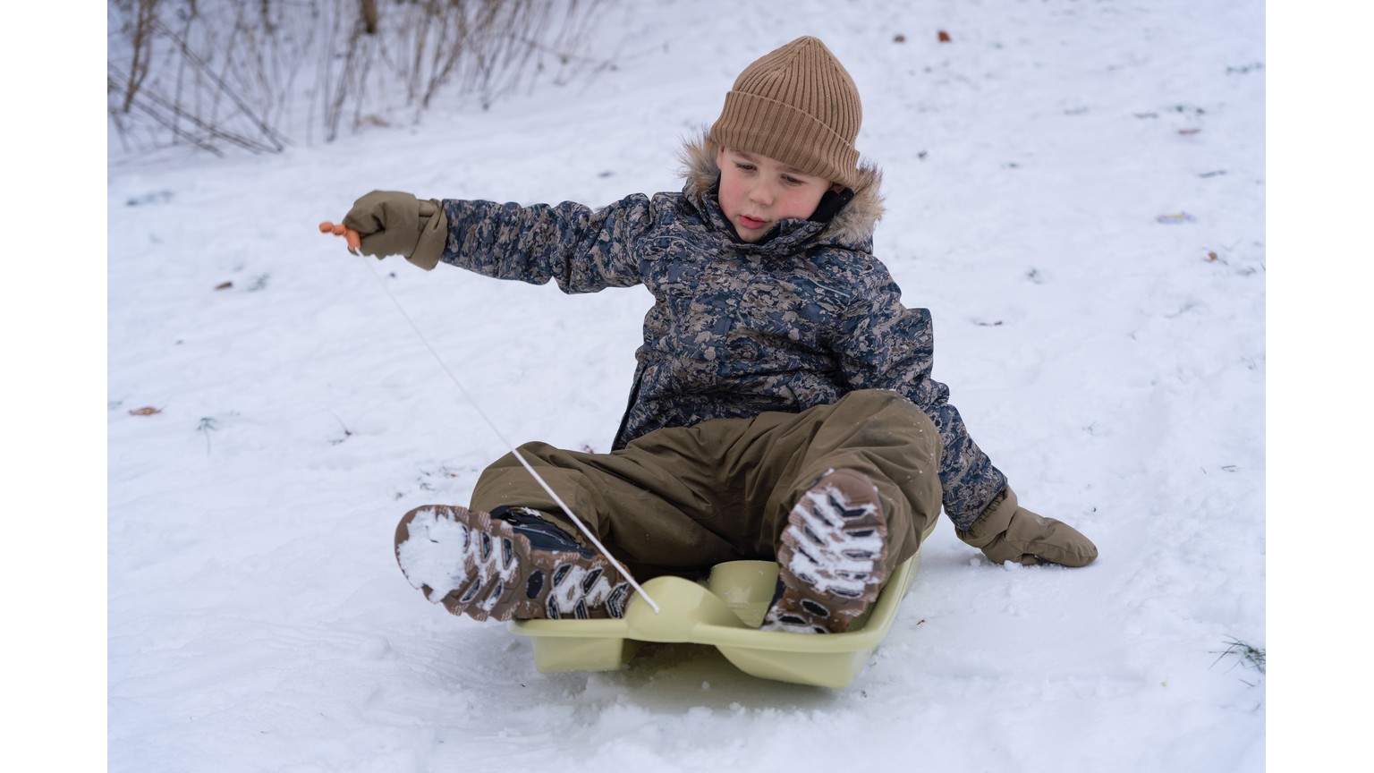 Barn på grøn slæde i snedækket landskab