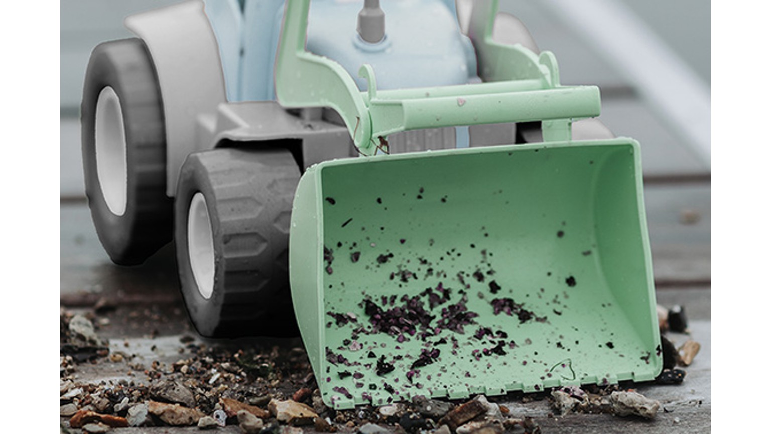 Grøn skovl monteret på mintgrøn traktor i leg med jord og mudder.
