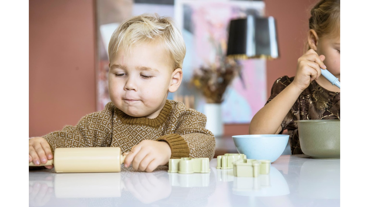 Barn ved bord med småt bageudstyr og dej foran sig