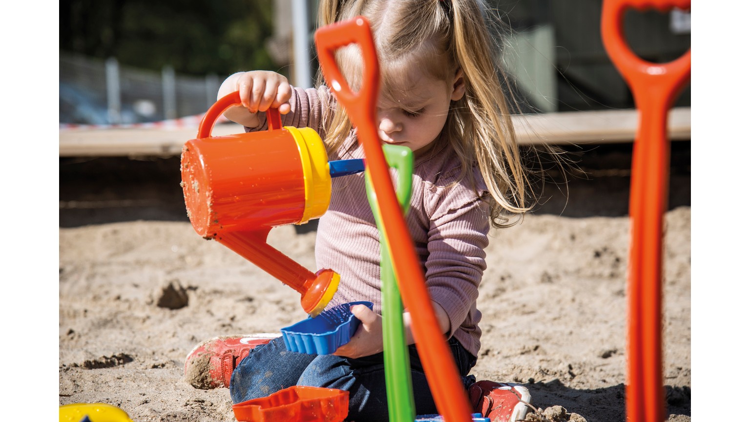 Gul vandkande og orange skovl bruges til sandleg i en sandkasse.