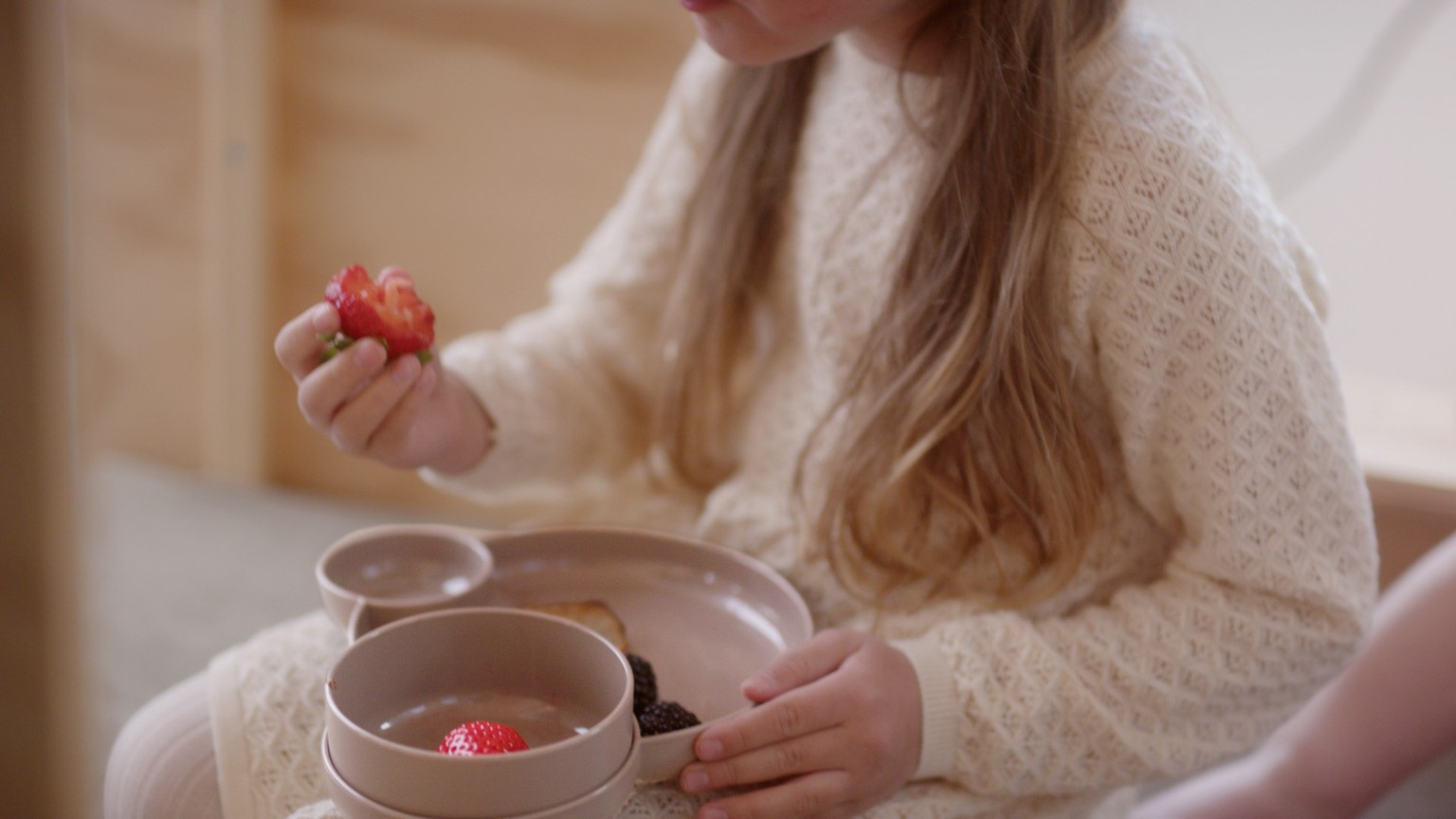Person i strikket sweater holder en kop med varm drik og et jordbær