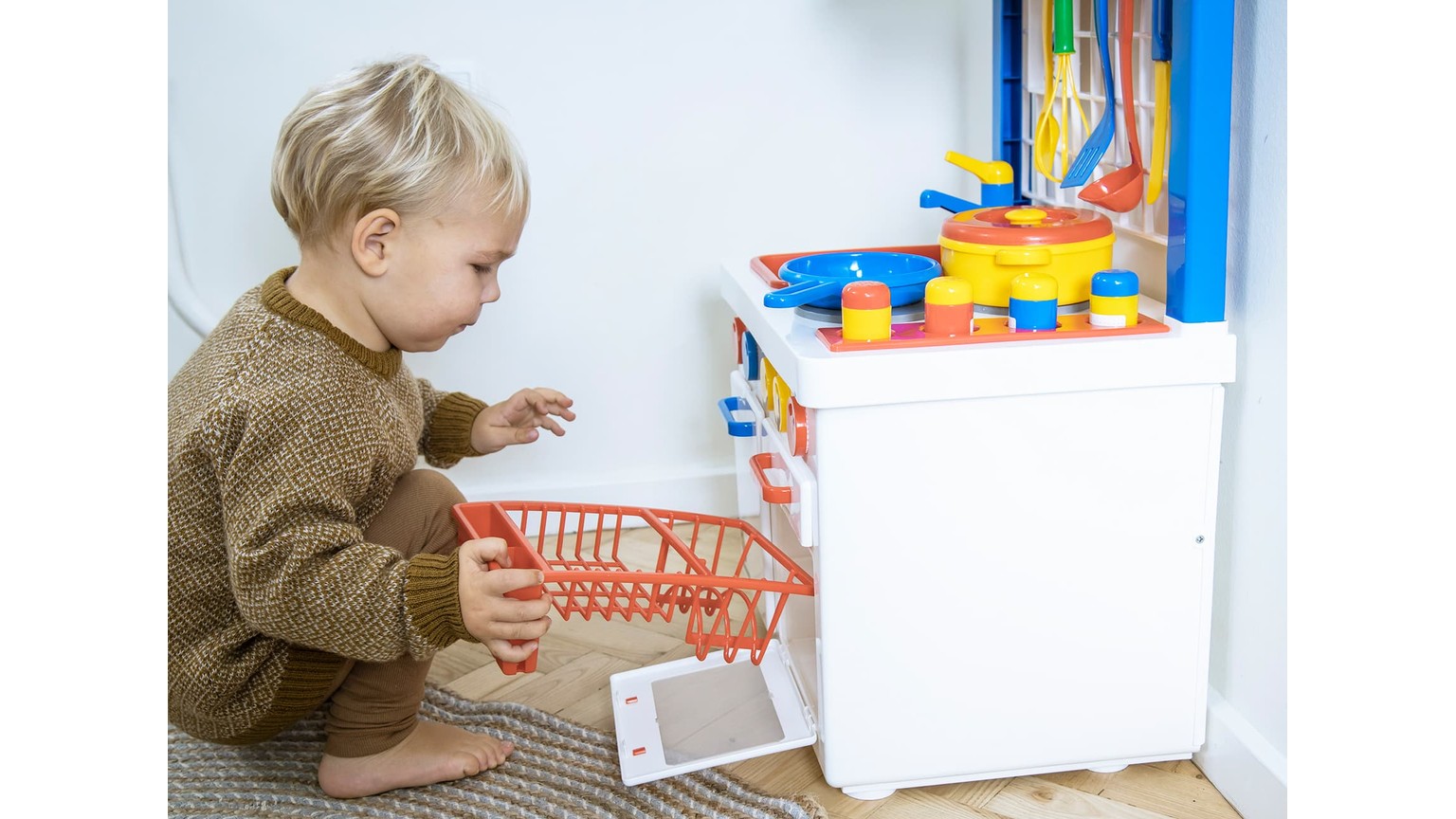 Barn leger med hvidt køkkenlegetøj med rød indkøbskurv og farverige elementer