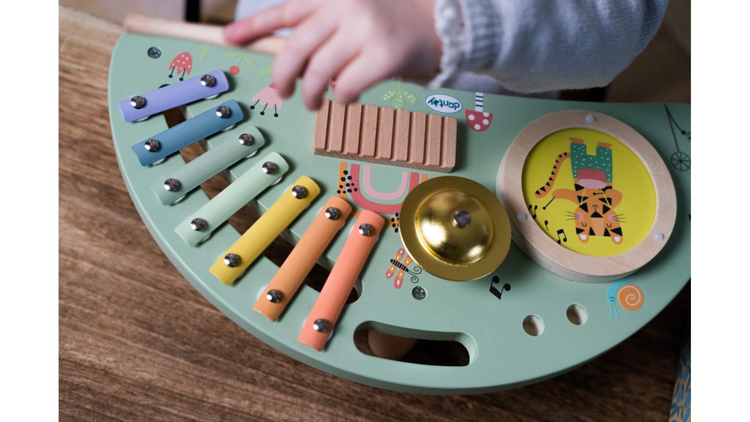 Farverigt musiklegetøj med xylofon og klokke på grøn halvmåneformet base på træbord.