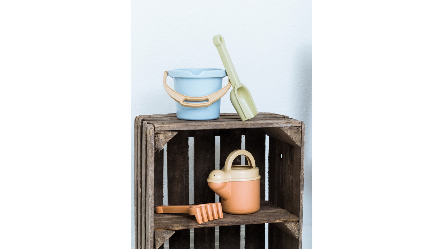 Blåt vandkande og orange blomsterpotte placeret på rustik trækasse med tremmer.