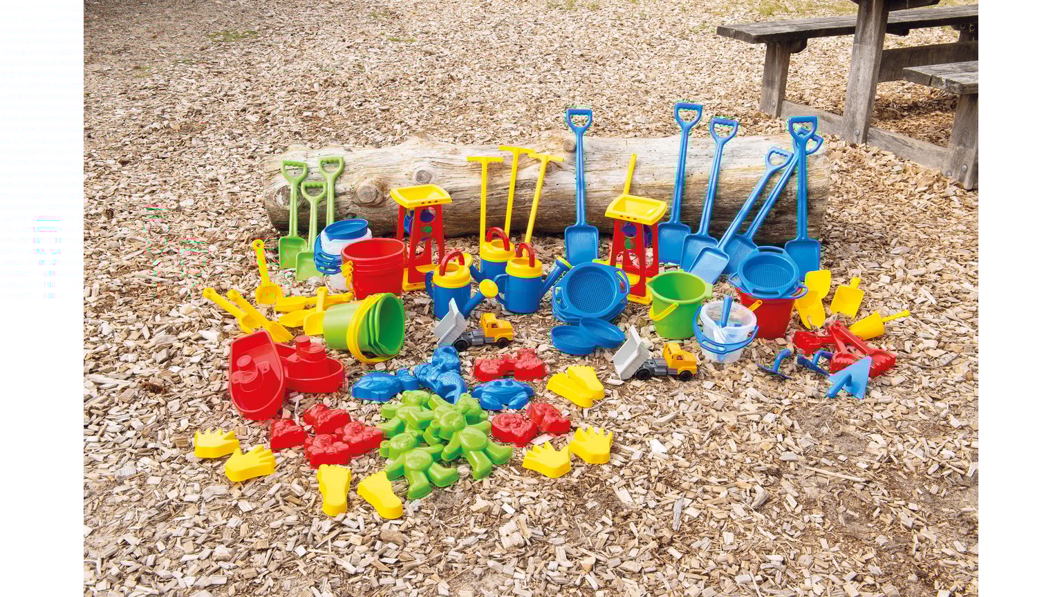 Farverigt sandlegetøjssæt med skovle, forme og spande spredt ud på sandunderlag