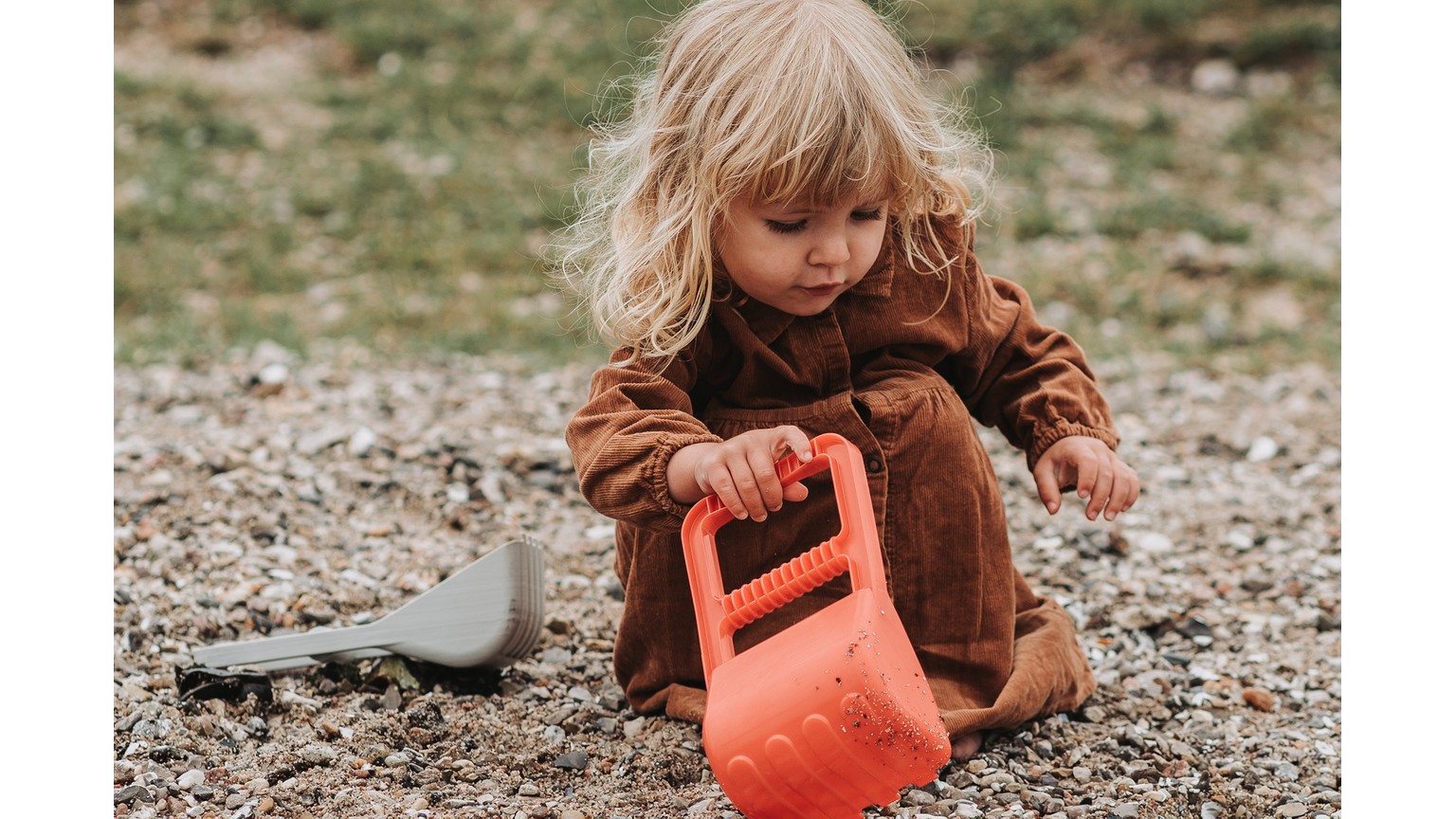 Barn i brun tøj leger med en orange vandkande på jorden