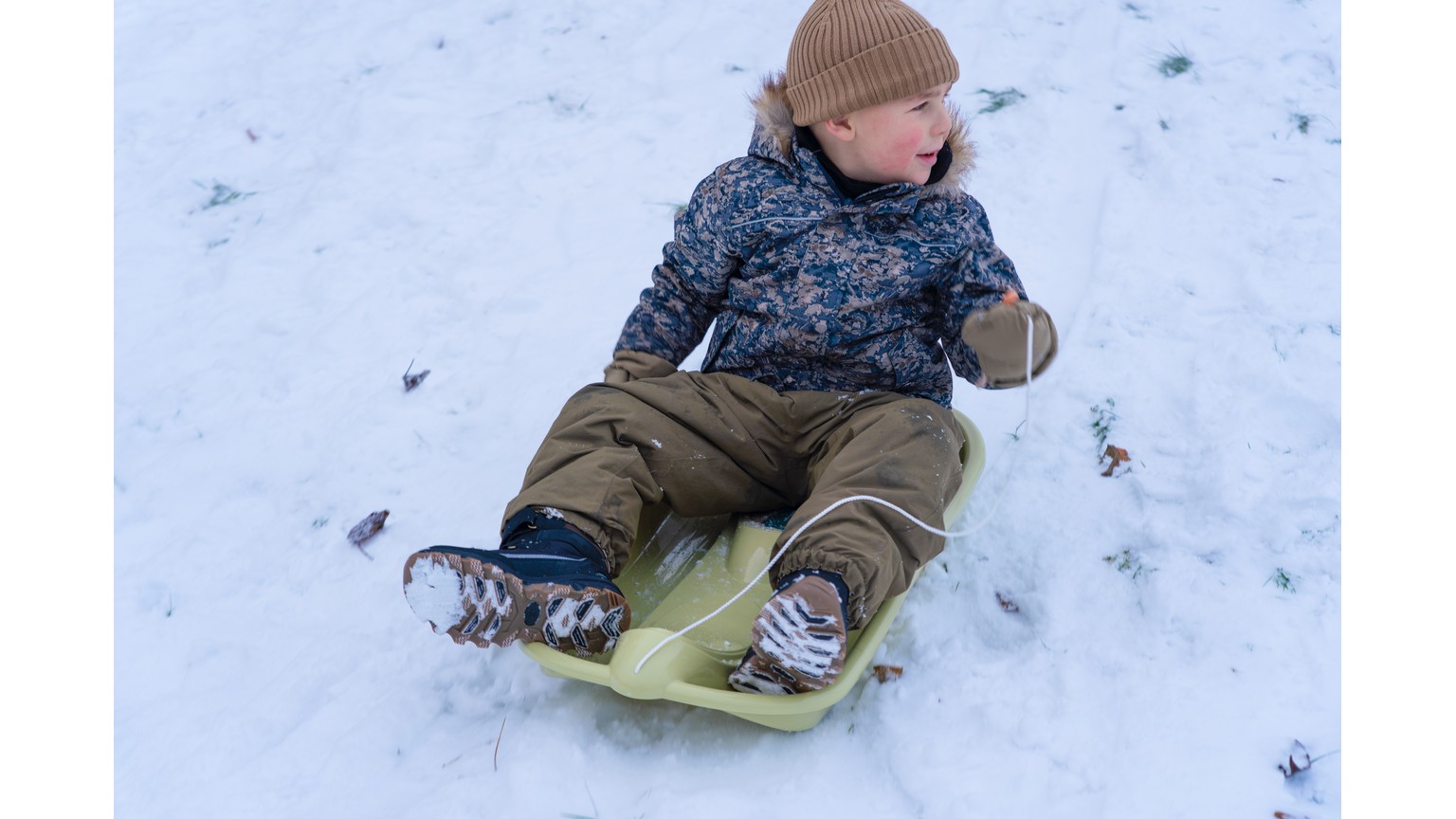 Barn på grøn bobslæde i sneen om vinteren