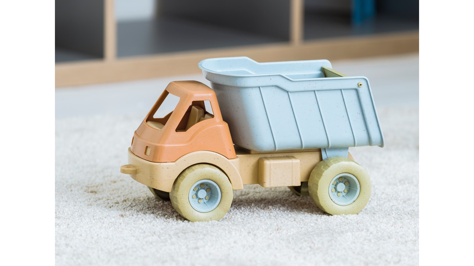 Lyseblå og beige legelastbil med tippelad på tæppe