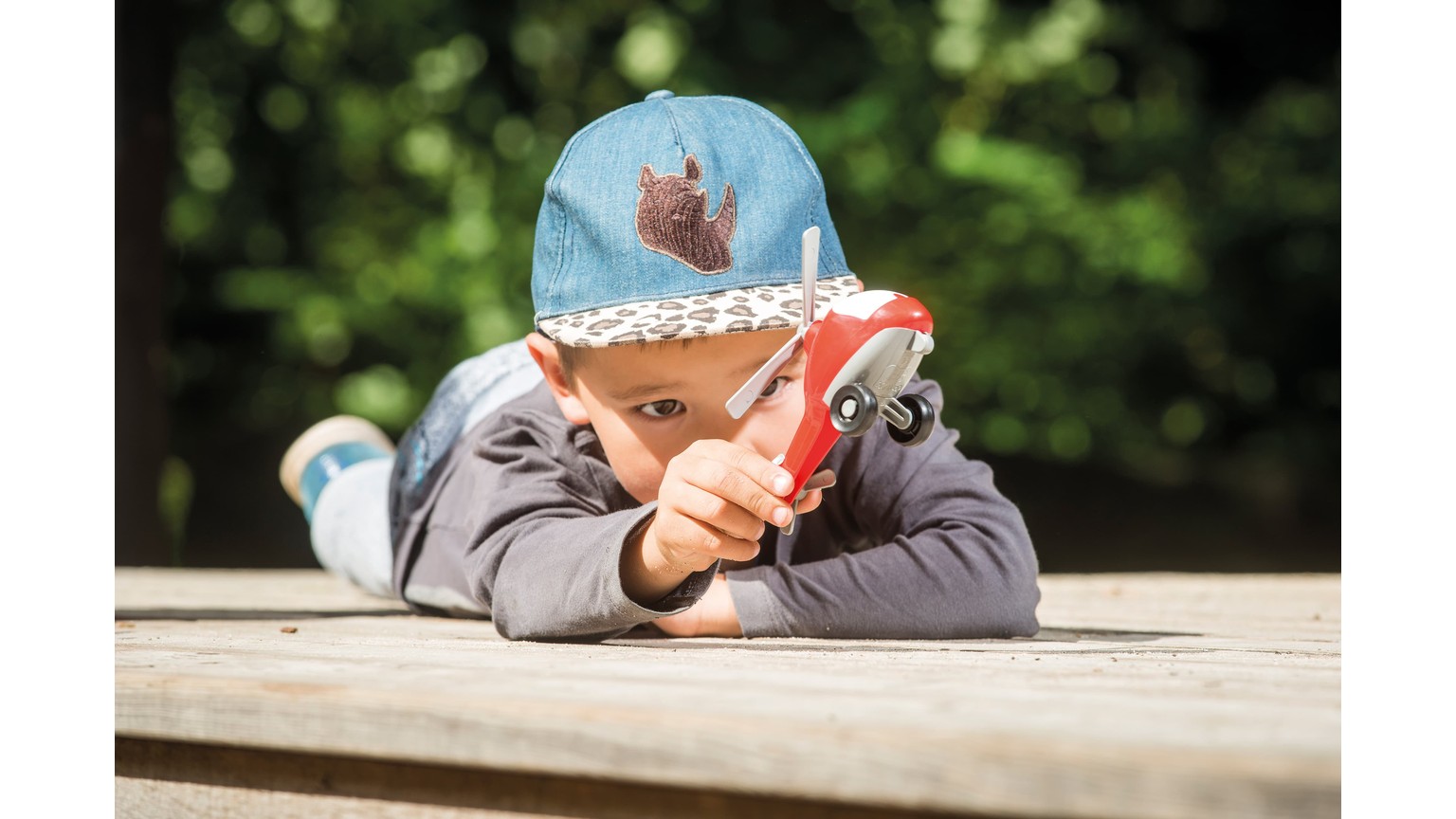 En lille person ligger på træbord med en rød bog, iført grå tøj og blå hue