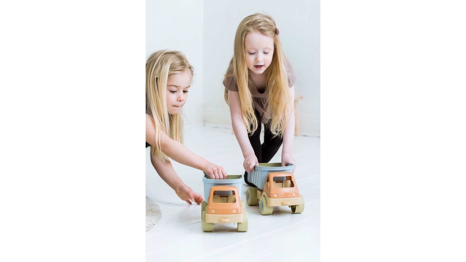 To børn leger med brune legelastbiler på hvidt gulv