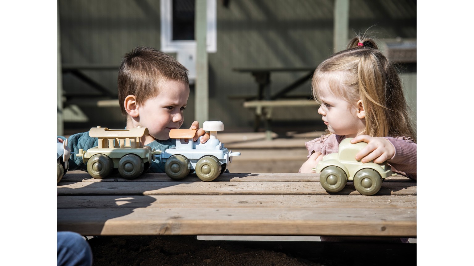 To børn leger med legetøjsbiler på et træbord.