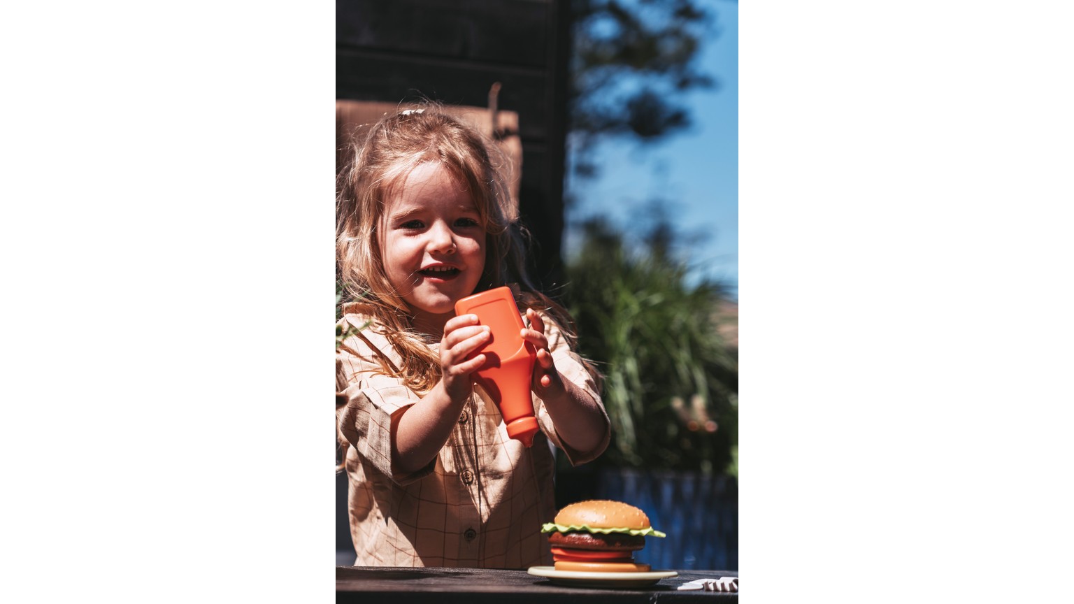 Et børnemåltid med stor hamburger og rød drikkevare på bord udendørs.