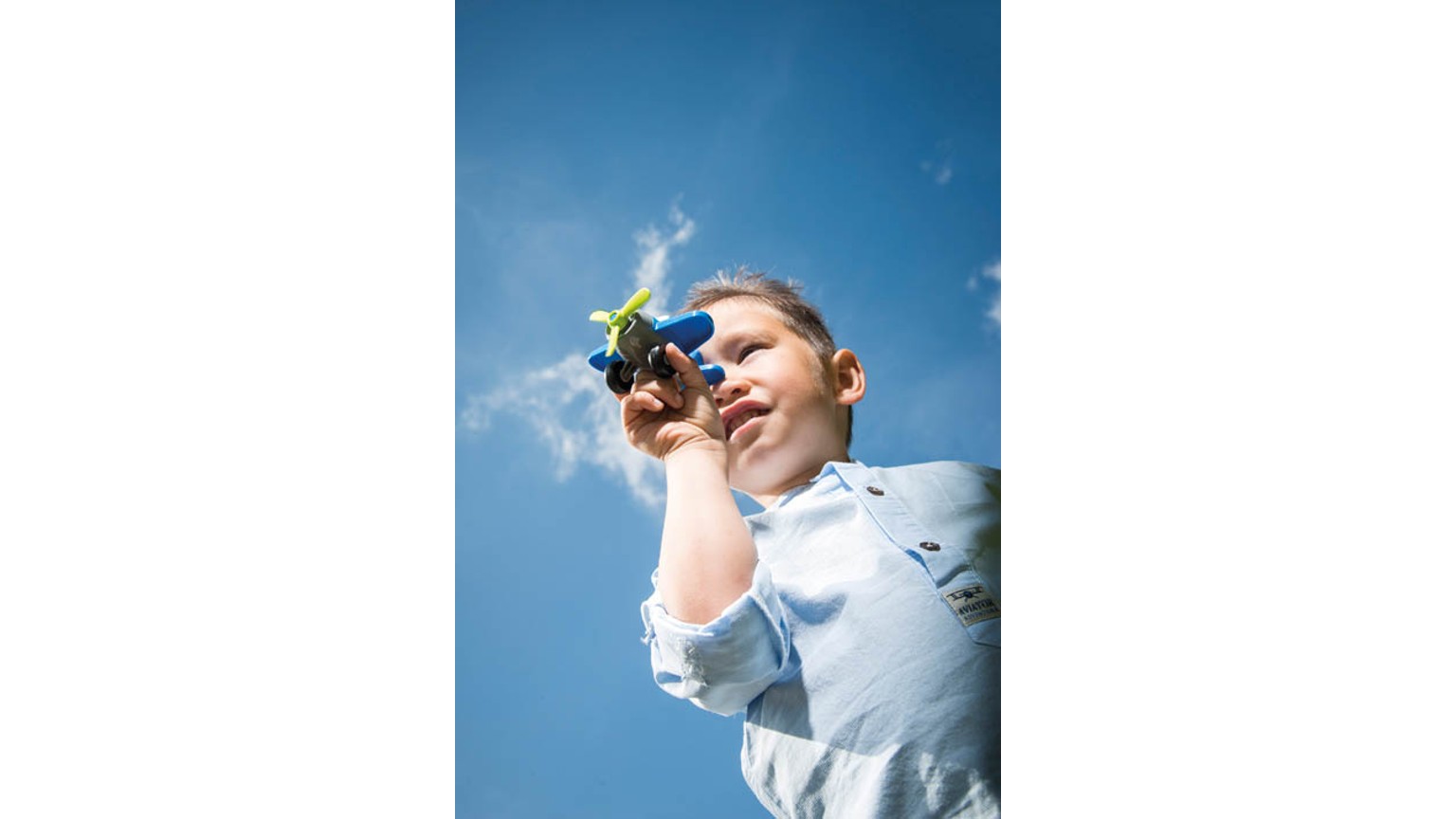Barn med gult legetøj mod en blå himmel på en solrig dag