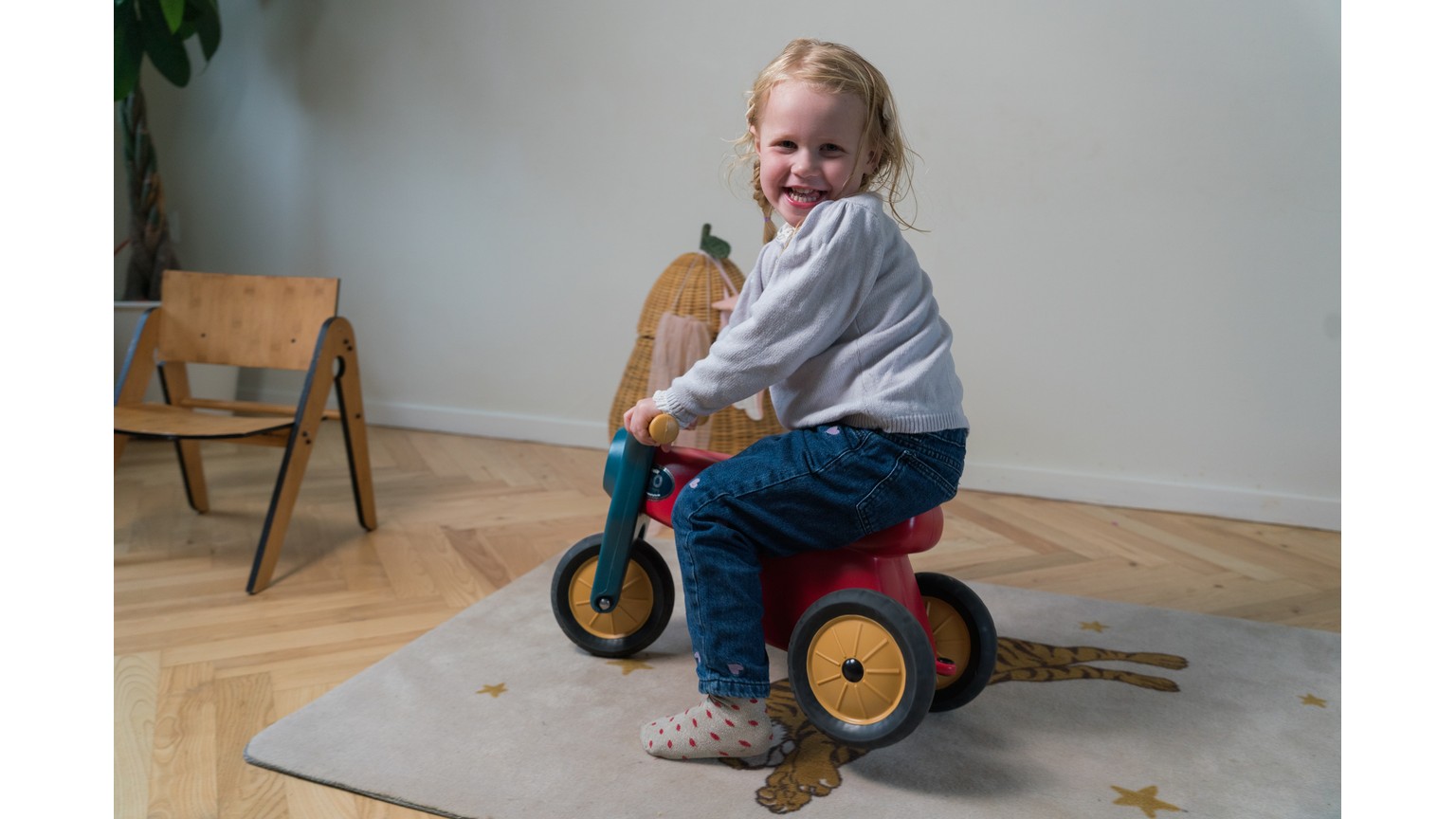 Barn på trehjulet motorcykel i blå og gul på trægulv ved stol